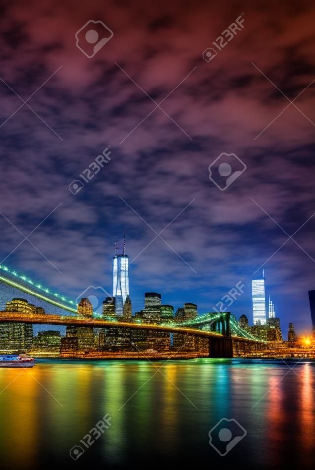 New York City Manhattan panorama view with Brooklyn Bridge at night with office building skyscrapers skyline illuminated over Hudson River.