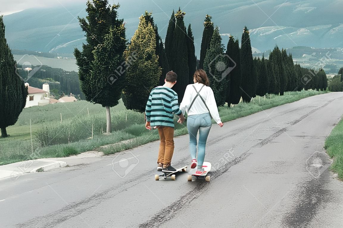 Giovani coppie che guidano uno skateboard su una strada. Concetto di millennial Skateboarder sui pattini