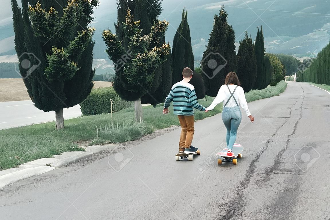 Jong stel met een skateboard op een weg. Concept van millenials Skateboarders op schaatsen