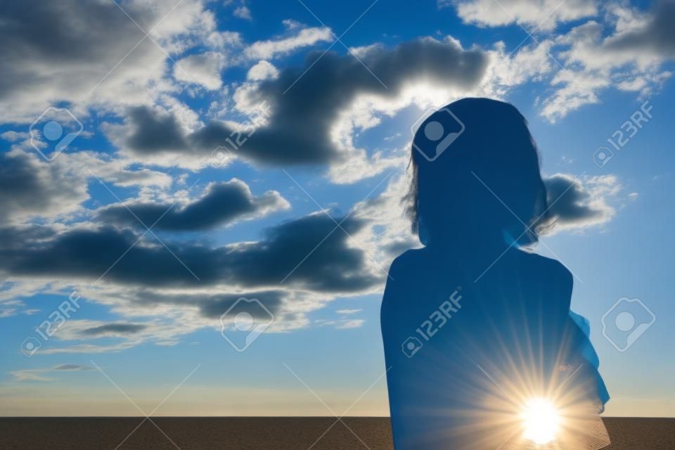 Lady silhouette against cloudy blue sky in the morning at the beach when sun rise, standing confident with shadow looking
