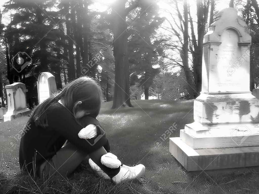 Una muchacha que se aflige está de luto en un cementerio, encrespado
para arriba delante de un sepulcro grande.