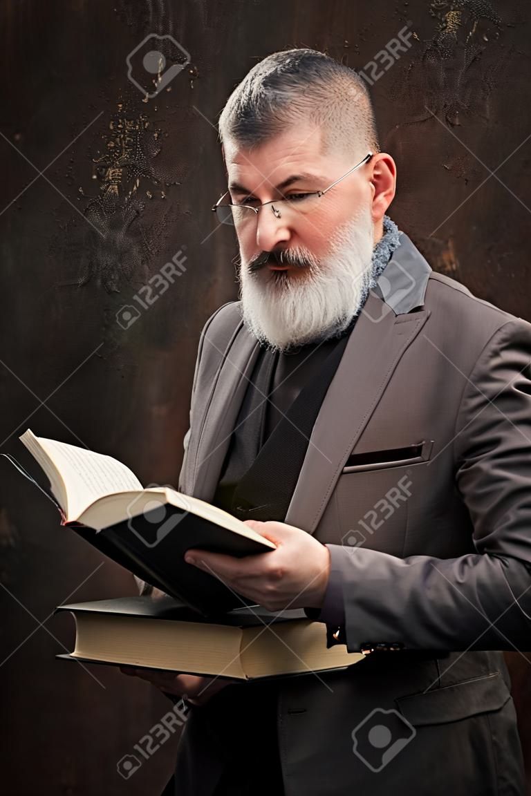 Portrait of a gray haired bearded man with glasses reading book in Russian, on the cover Russian inscription M. Gorky, selective focus