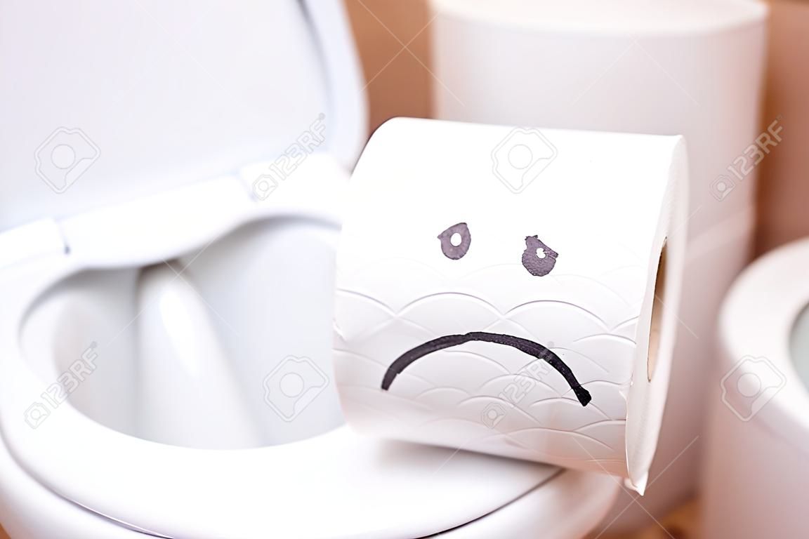 Close-up van een rol wc-papier met een geschilderd droevig gezicht staat op het toilet