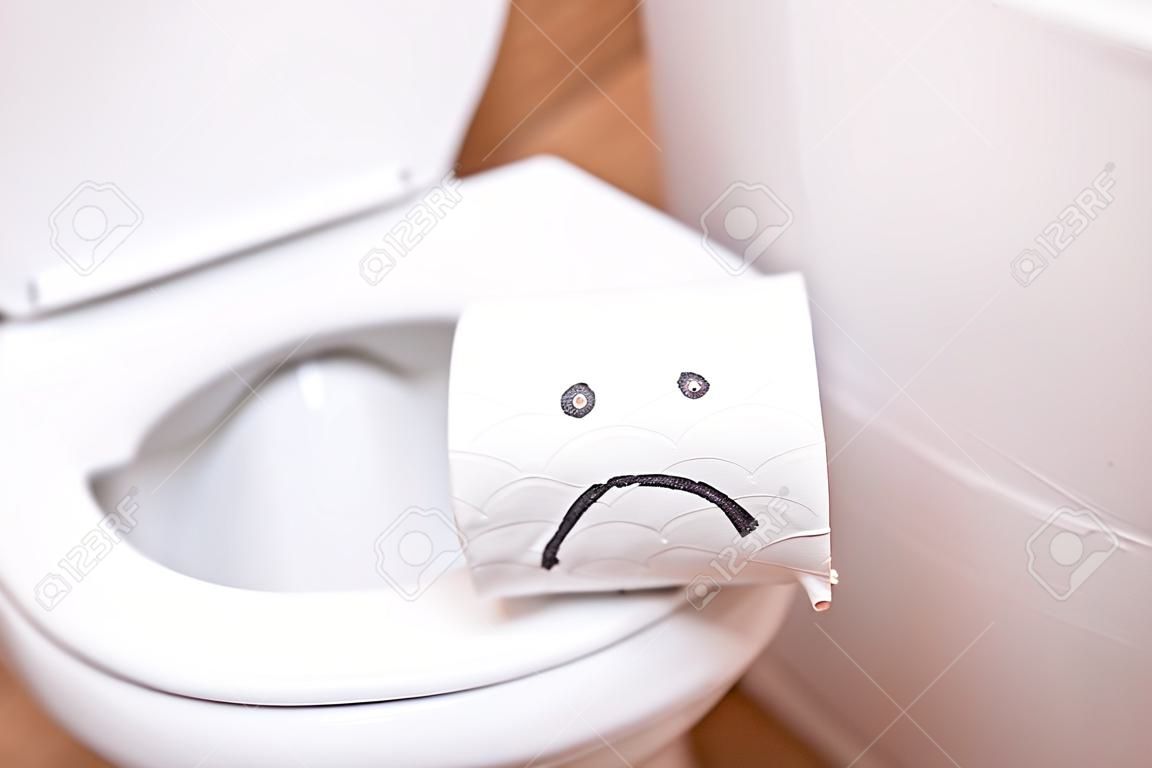 Close-up van een rol wc-papier met een geschilderd droevig gezicht staat op het toilet
