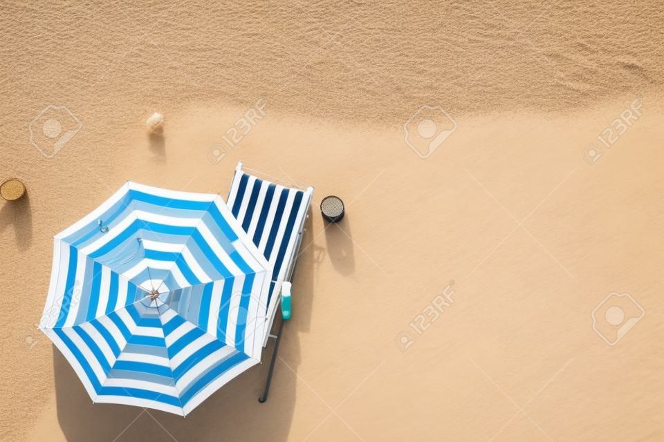 夏休みのコンセプト。砂浜の傘の下にあるサンラウンジャーのトップビュー