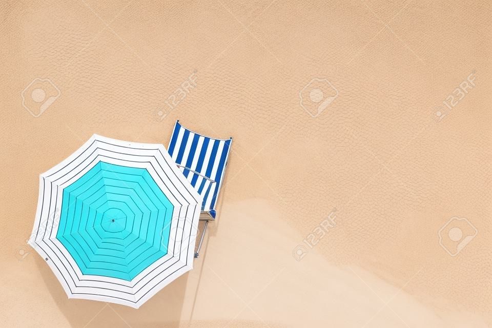 夏休みのコンセプト。砂浜の傘の下にあるサンラウンジャーのトップビュー