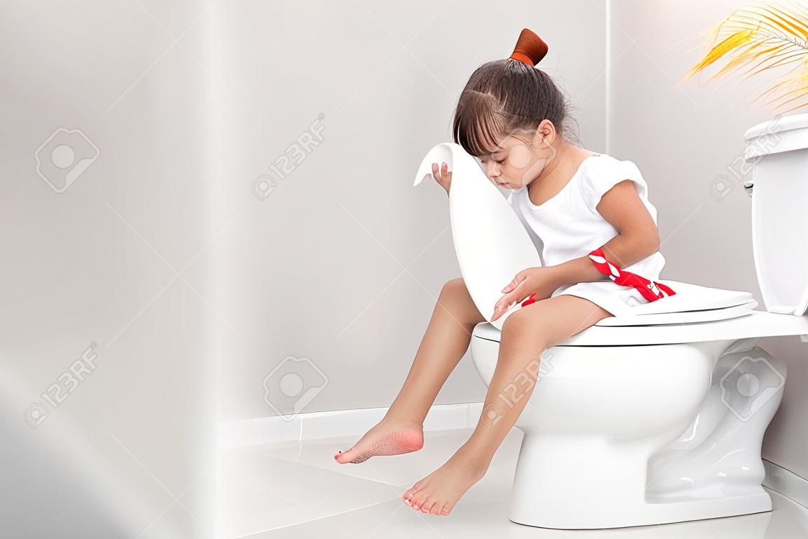 La bambina è seduta sul water e soffre di stitichezza o emorroidi.