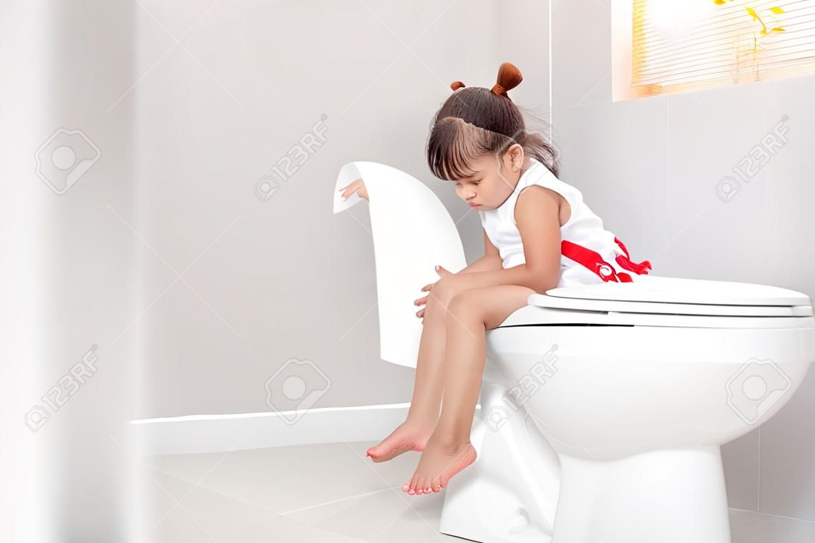 La niña está sentada en el baño sufriendo de estreñimiento o hemorroides.