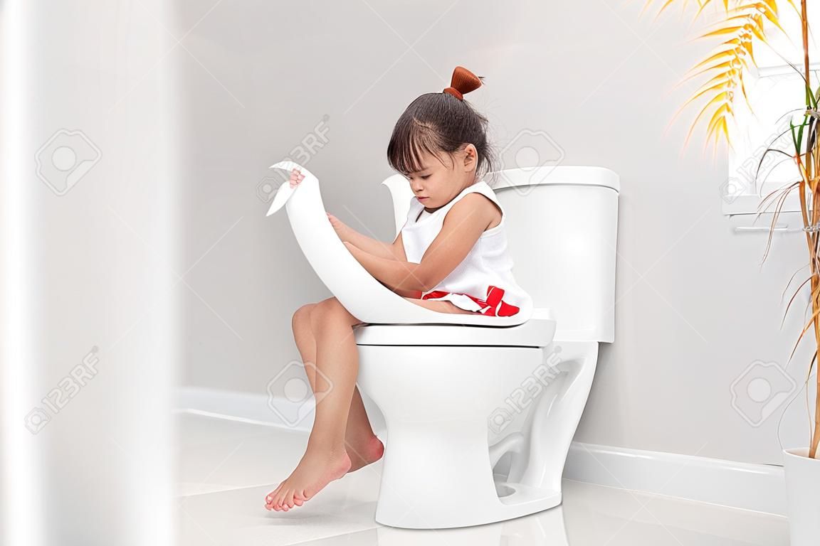 La niña está sentada en el baño sufriendo de estreñimiento o hemorroides.