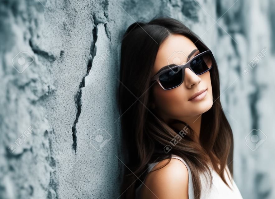 Belle femme brune avec des lunettes de soleil sur un mur en ruine