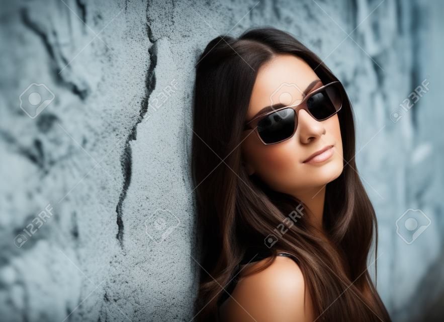 Beautiful brunette woman with sunglasses over a ruinous wall