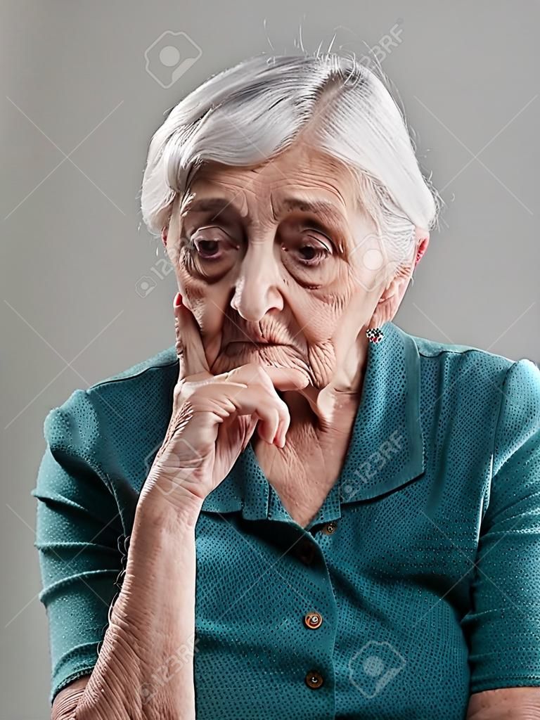 Retrato de la mujer mayor en un estudio de disparo. Mujer de edad tenía su mano en la barbilla y triste