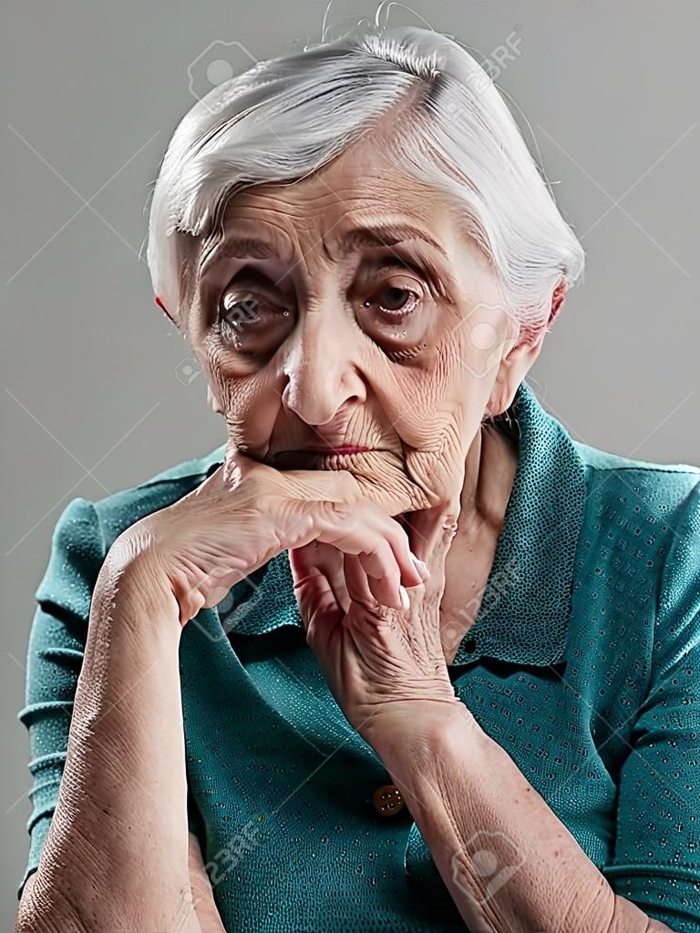 Retrato da mulher idosa em um tiro do estúdio. A mulher velha teve sua mão no queixo e triste