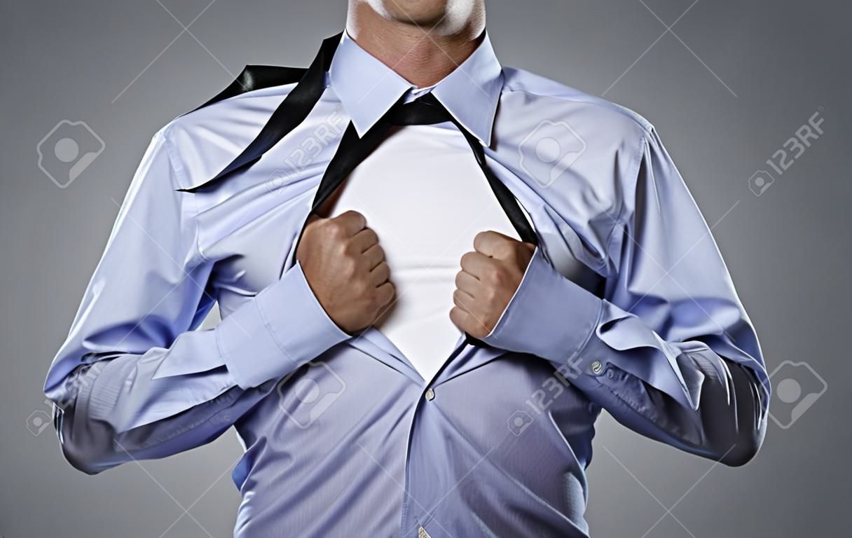 Молодой бизнесмен рвал на себе рубашку, изолированных на сером фоне с копией пространства