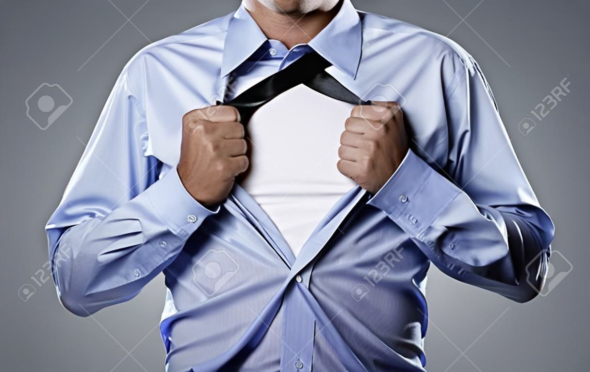 Jeune homme d'affaires déchirer sa chemise hors isolé sur fond gris avec copie espace