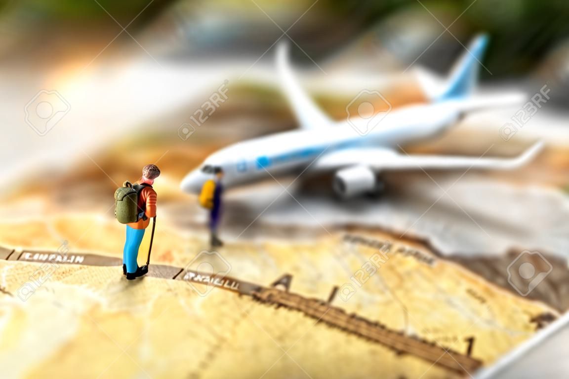 Persone in miniatura: viaggiare con uno zaino in piedi su mappa del mondo vintage e aereo, concetto di viaggio e vacanza.