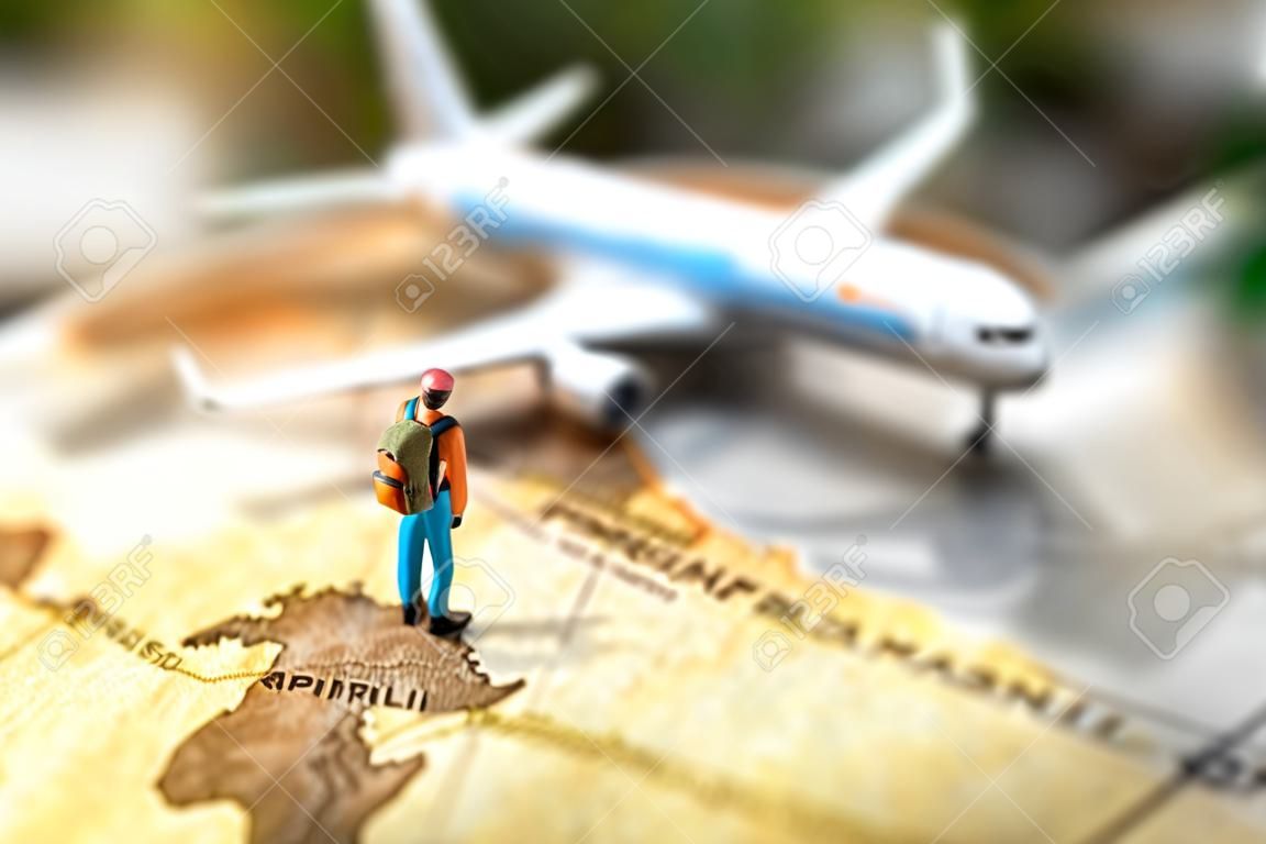 Persone in miniatura: viaggiare con uno zaino in piedi su mappa del mondo vintage e aereo, concetto di viaggio e vacanza.