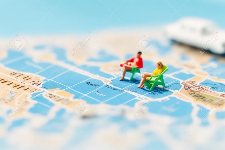 미니어처 사람들은 빈티지 세계 지도와 배, 여름 컨셉의 해변 일광욕 의자에 앉아 있습니다.