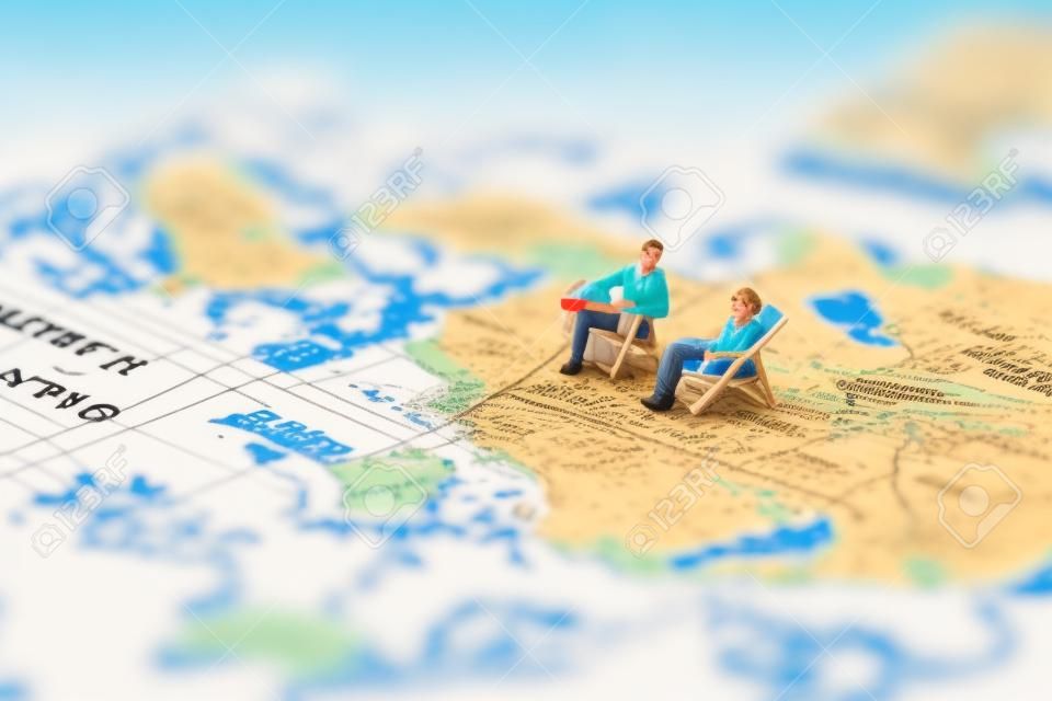 미니어처 사람들은 빈티지 세계 지도와 배, 여름 컨셉의 해변 일광욕 의자에 앉아 있습니다.