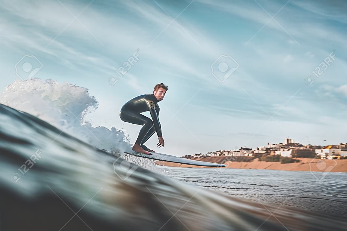 Handsome young man rides a wave off the coast with his surfboard. Extreme water sports and outdoor active lifestyle. Vintage filter with soft style