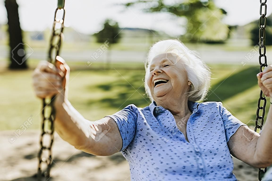 Mujer mayor alegre en un columpio en un patio de recreo