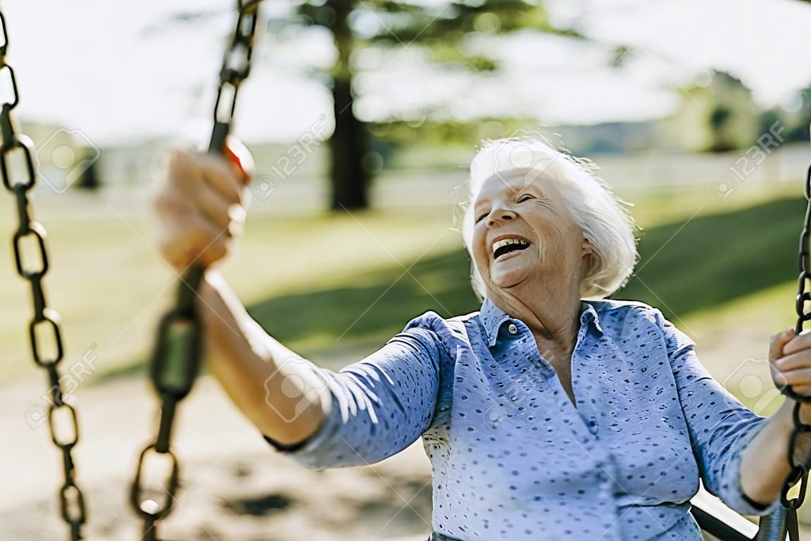 Mujer mayor alegre en un columpio en un patio de recreo