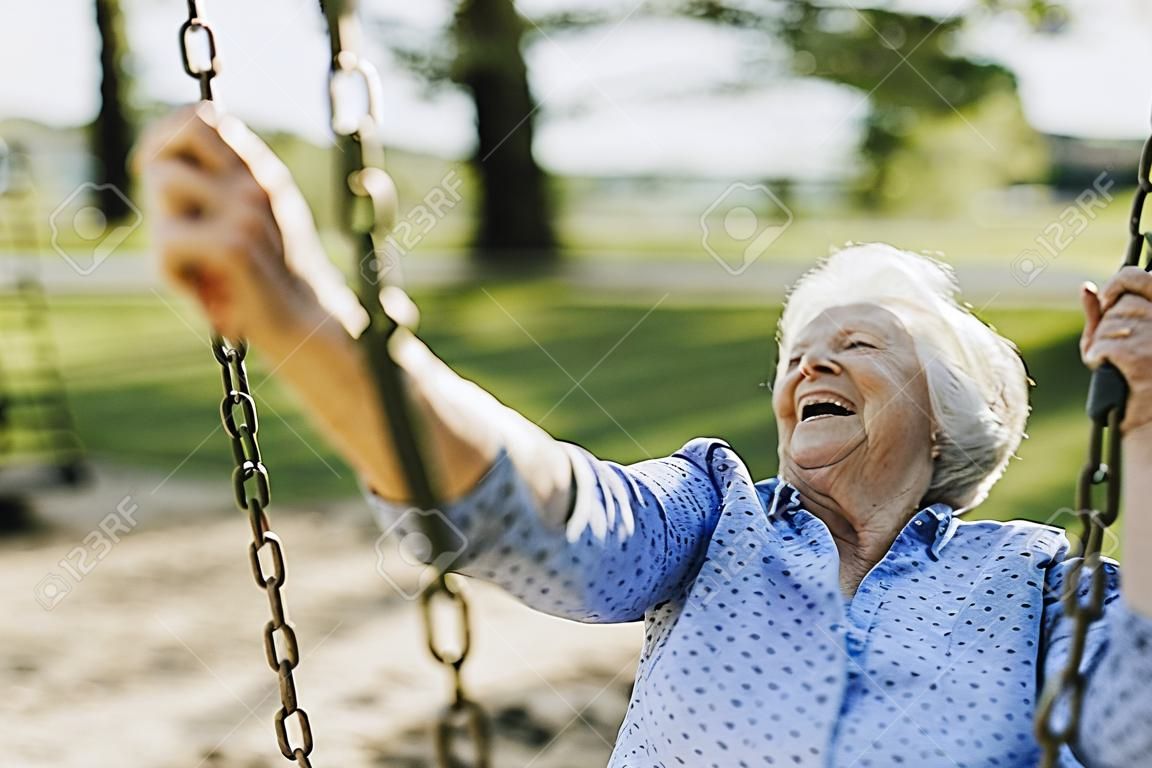 Cheerful senior woman sur une balançoire dans une aire de jeux