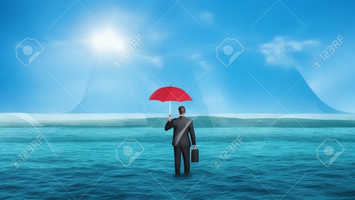 Geschäftsmann, der mit einem Regenschirm im Ozean steht