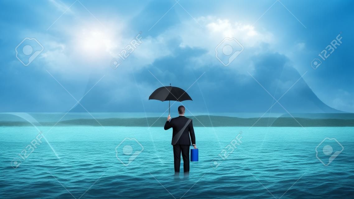 Geschäftsmann, der mit einem Regenschirm im Ozean steht