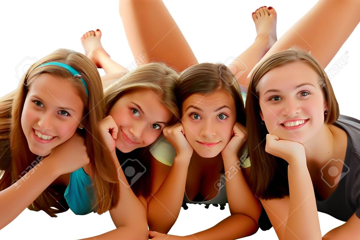 Three teenage girls laying on their stomach on the floor with chin in hands, and feet raised up and crossed behind them on white background in studio.