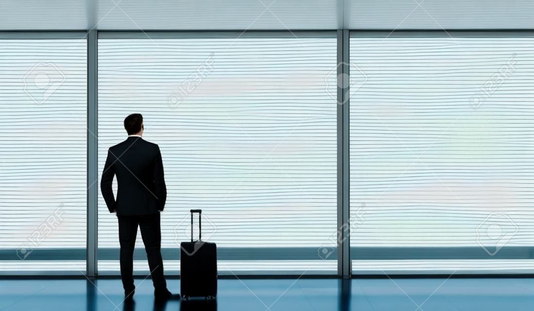 Mann steht und schaut aus dem Flughafenfenster, während er auf den Abflug wartet