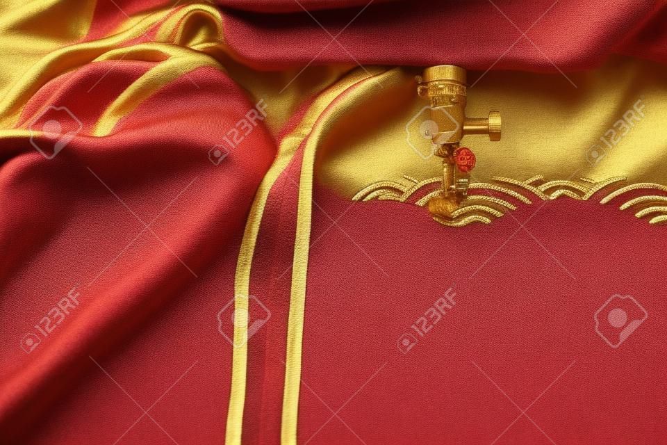 Embroidery of traditional shell pattern with gold on red fabric by modern embroidery machine - chinese new year concept - view on machine head, sewing foot and hoop at process of satin stitch in bright light