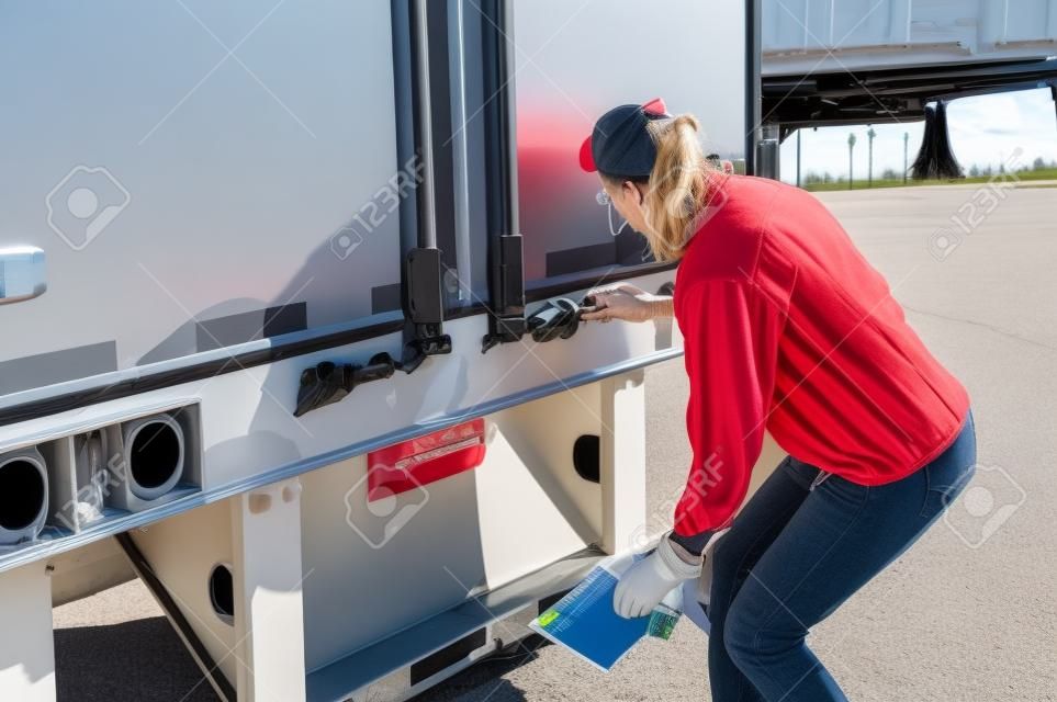 Woman truck driver checking her trailer seal number to make sure it matches the numbers on her bill of lading.