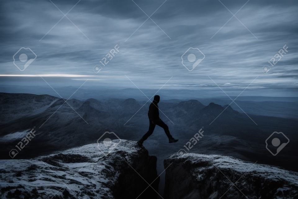 Caminhante louco em preto está pulando entre picos rochosos. Homem feliz. Maravilhoso amanhecer em montanhas rochosas, névoa laranja pesada no vale profundo. Milagre da natureza