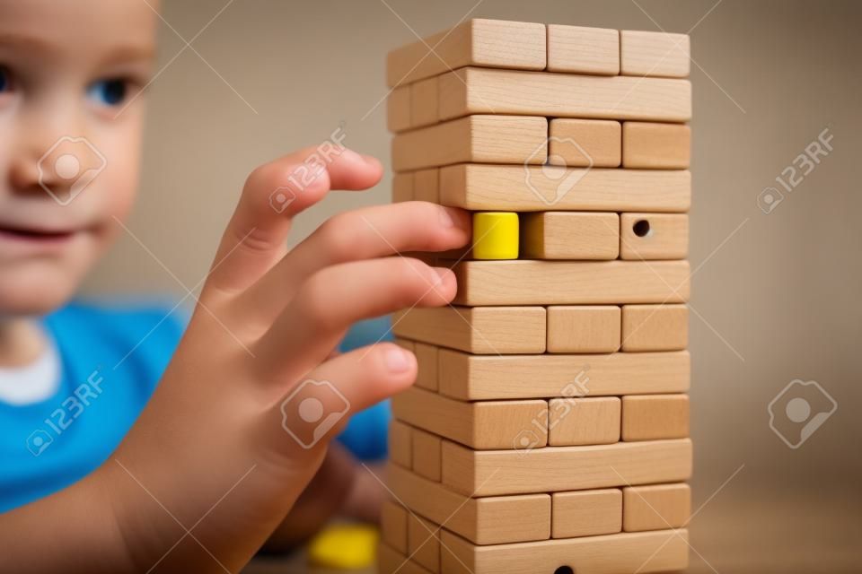 A preteen caucasian boy playing wooden block tower board game for practicing his physical and mental skill and entertainment.