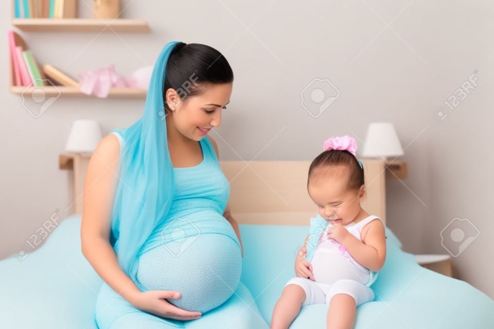 mother and her baby daughter waiting for newborn and showing tummies (focus on baby girl)