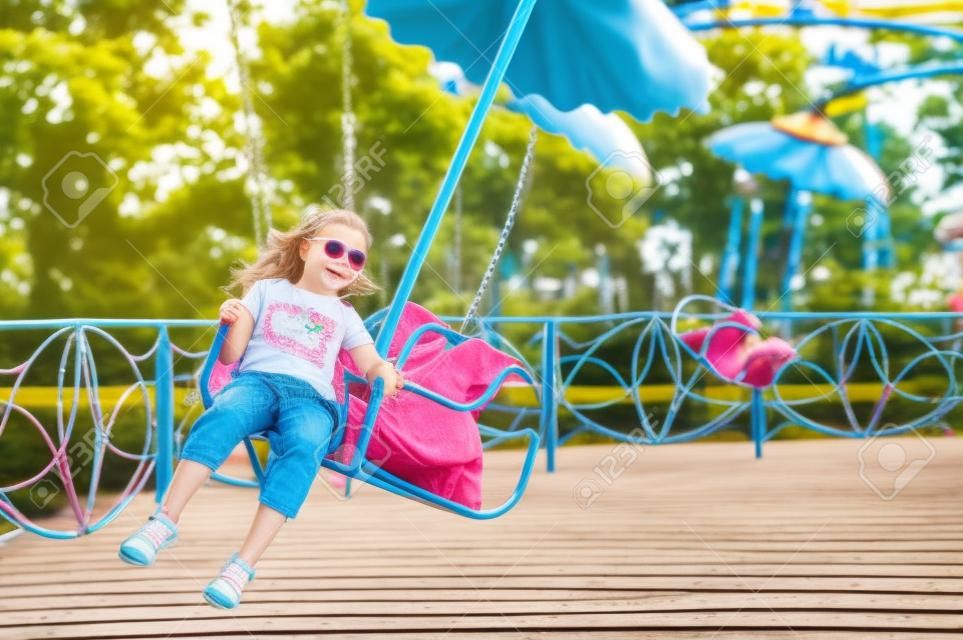 little girl  on the  chain swing ride, amusement park in summer