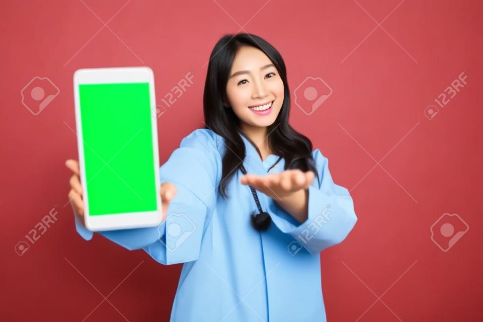 Young Asian woman doctor is smiling and showing green screen or copy space on her smartphone