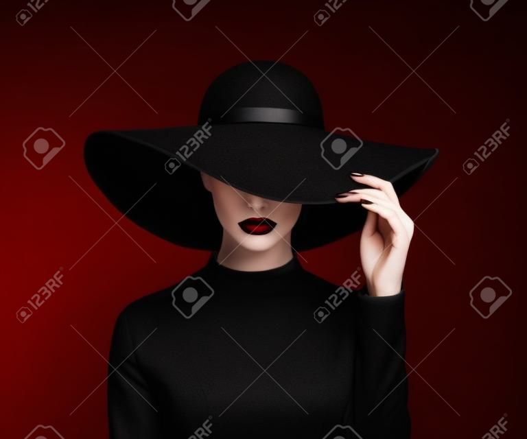 Mujer de lujo en un gran sombrero negro y los labios brillantes sobre fondo negro