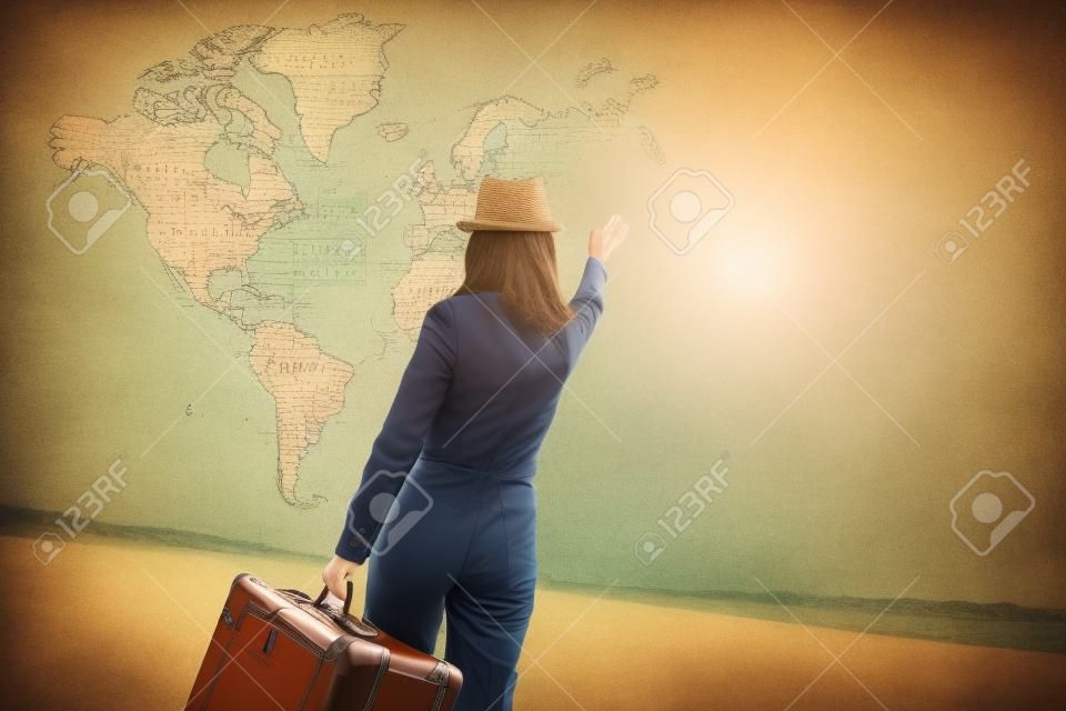Traveler woman with vintage suitcase waves her hand to map of the world. Concept of travel
