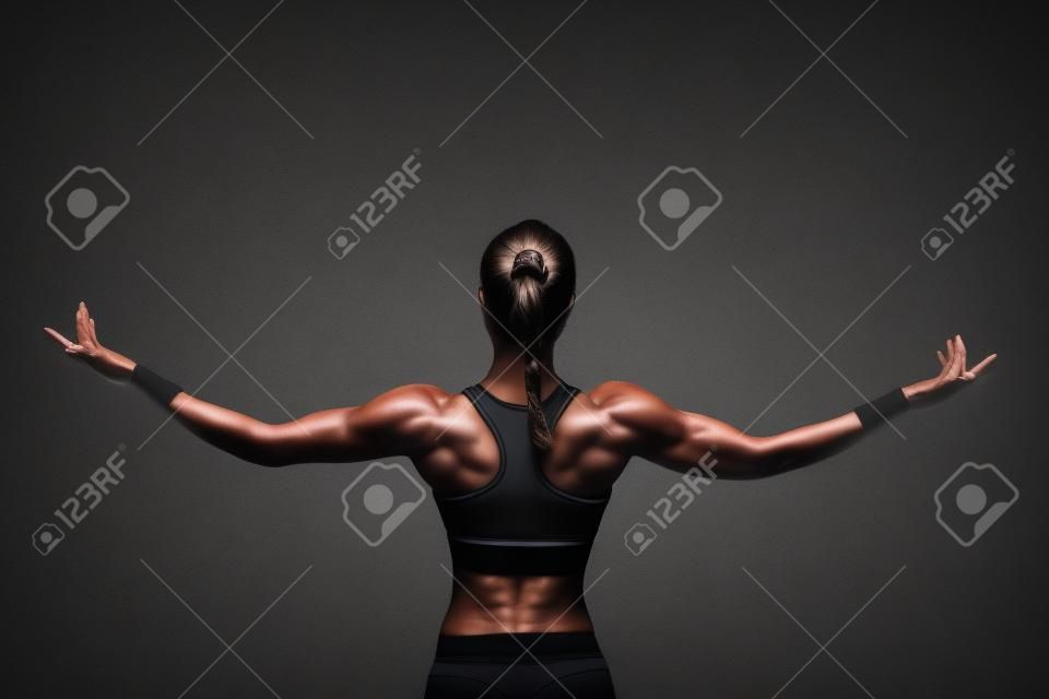 Athletic young woman showing muscles of the back and hands on a isolated black background