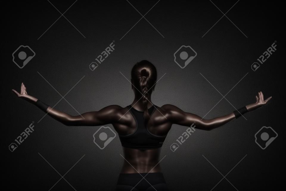 Atletische jonge vrouw tonen spieren van de rug en handen op een geïsoleerde zwarte achtergrond