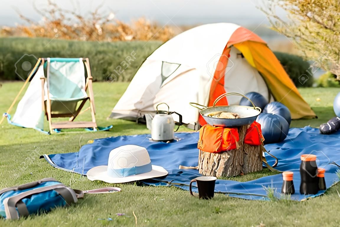 Camping place with tent, backpacks, chair and hiking equipmment outdoors on the green lawn