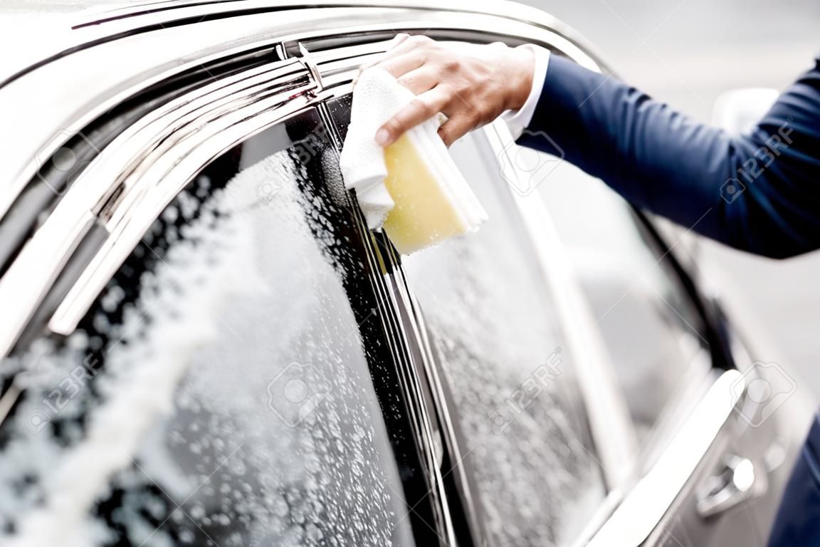 Businessman washing car window with sponge and foam on a self service car wash, close-up view with no face