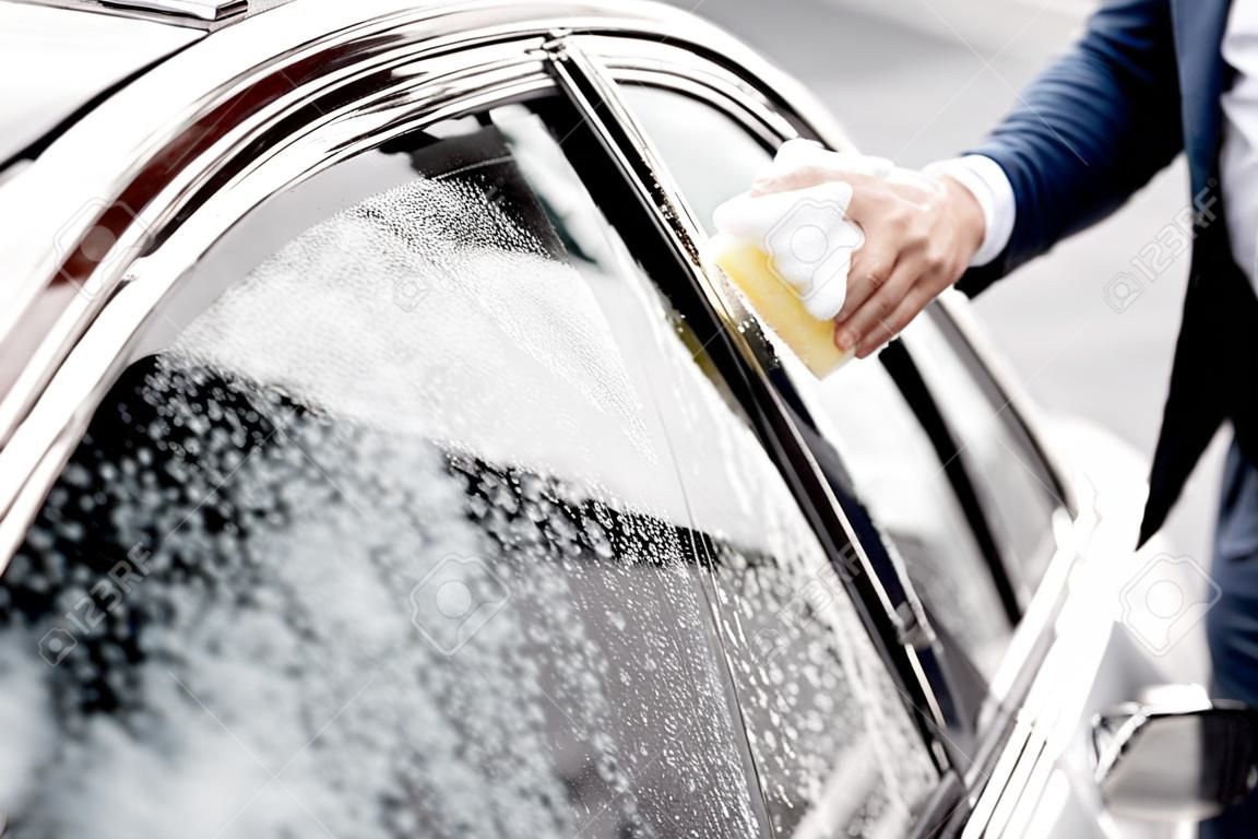 Empresario lavar la ventana del coche con esponja y espuma en un autoservicio de lavado de coches, vista cercana sin rostro
