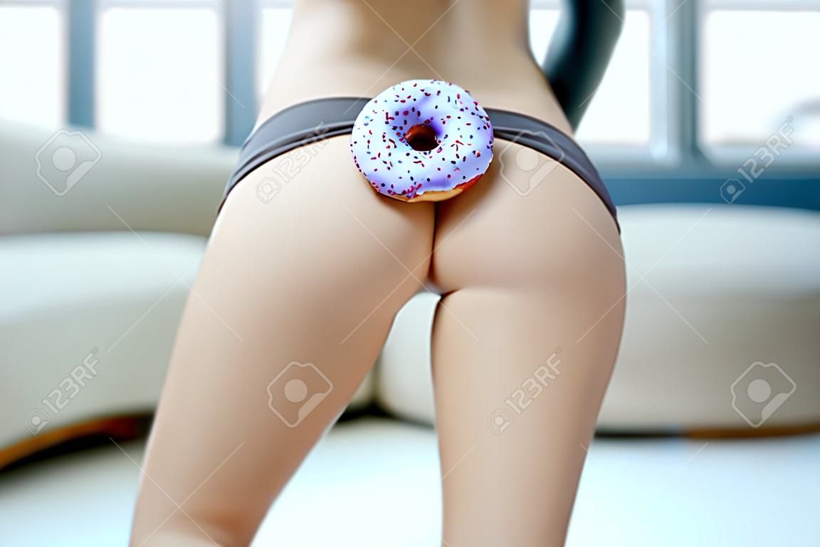 Close-up of a beautiful slim womens body with sweet donut indoors, weight loss and unhealthy eating concept