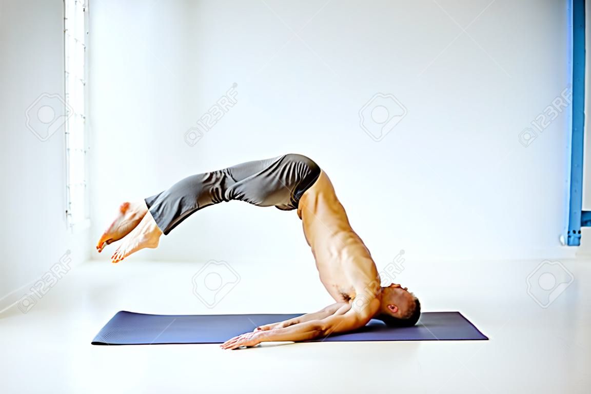 Senior athletic man with exposed torso practising yoga poses in the white studio
