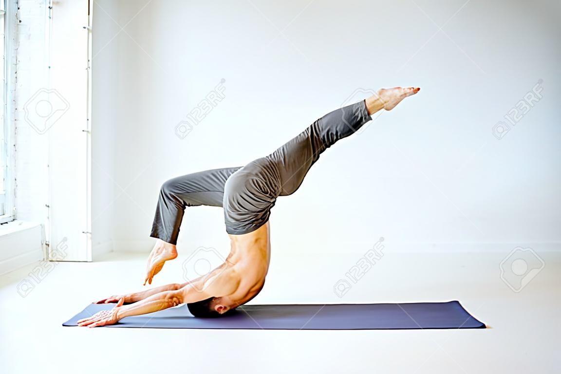 Senior athletic man with exposed torso practising yoga poses in the white studio