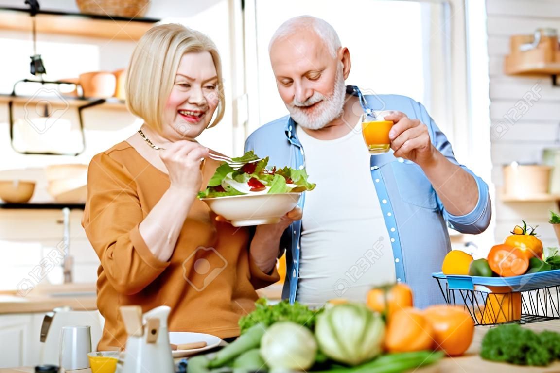 Porträt eines fröhlichen Seniorenpaares mit Salat und gesundem Essen in der Küche zu Hause. Konzept der gesunden Ernährung im Alter