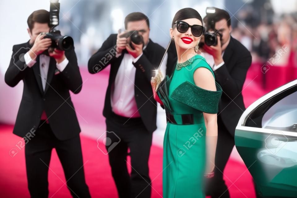 Bella donna vestita in stile retrò come una famosa attrice cinematografica che arriva alla cerimonia di premiazione con i fotoreporter che la fotografano